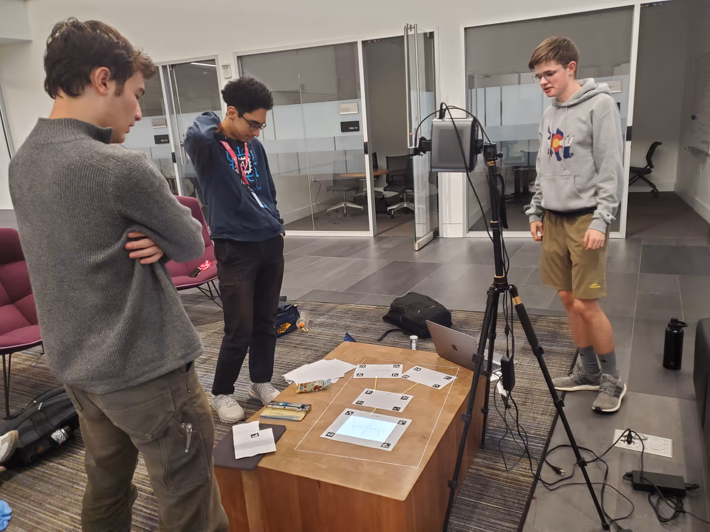 Three students look at a desk with a tripod holding a projector on it