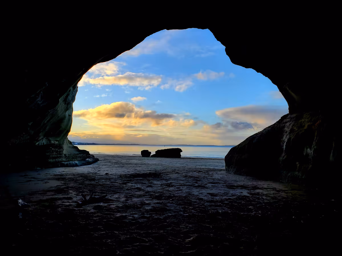 sunset over the ocean seen from inside a cave on the beach