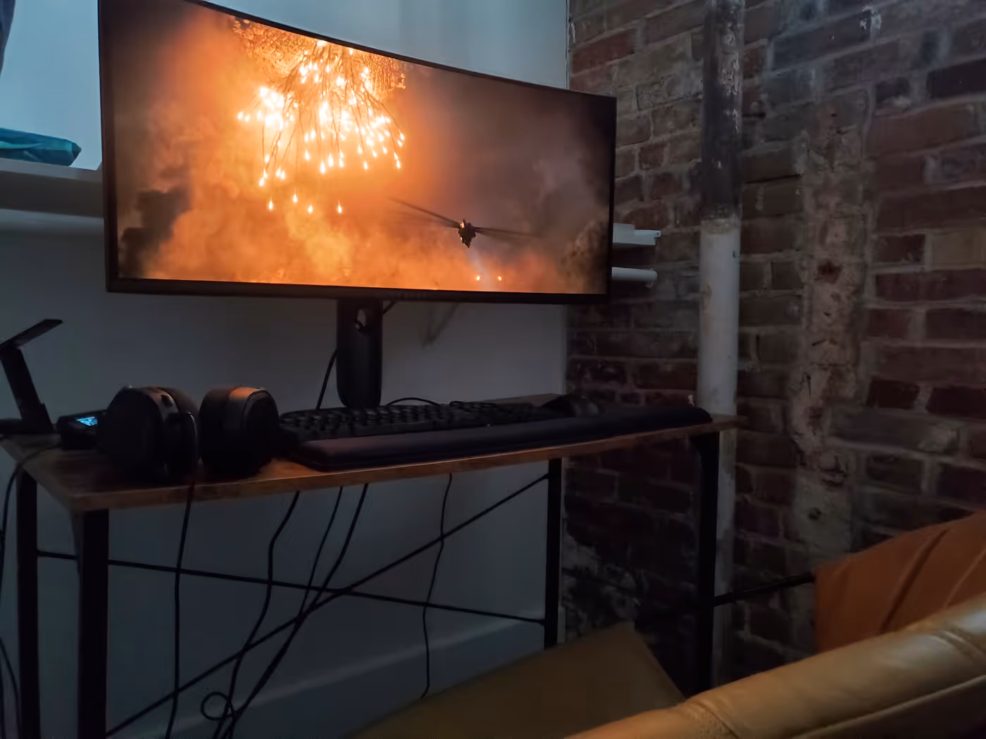 "a closet with brick walls and a PC setup with a monitor showing an explosion from the movie Dune: Part One"