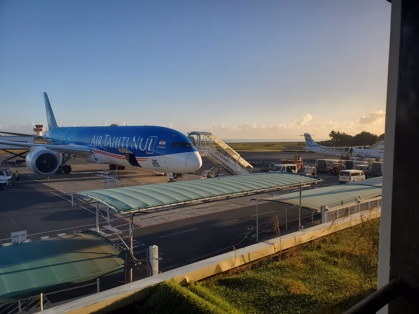 a Boeing 787 in Air Tahiti Nui livery parked on the airport tarmac at sunrise