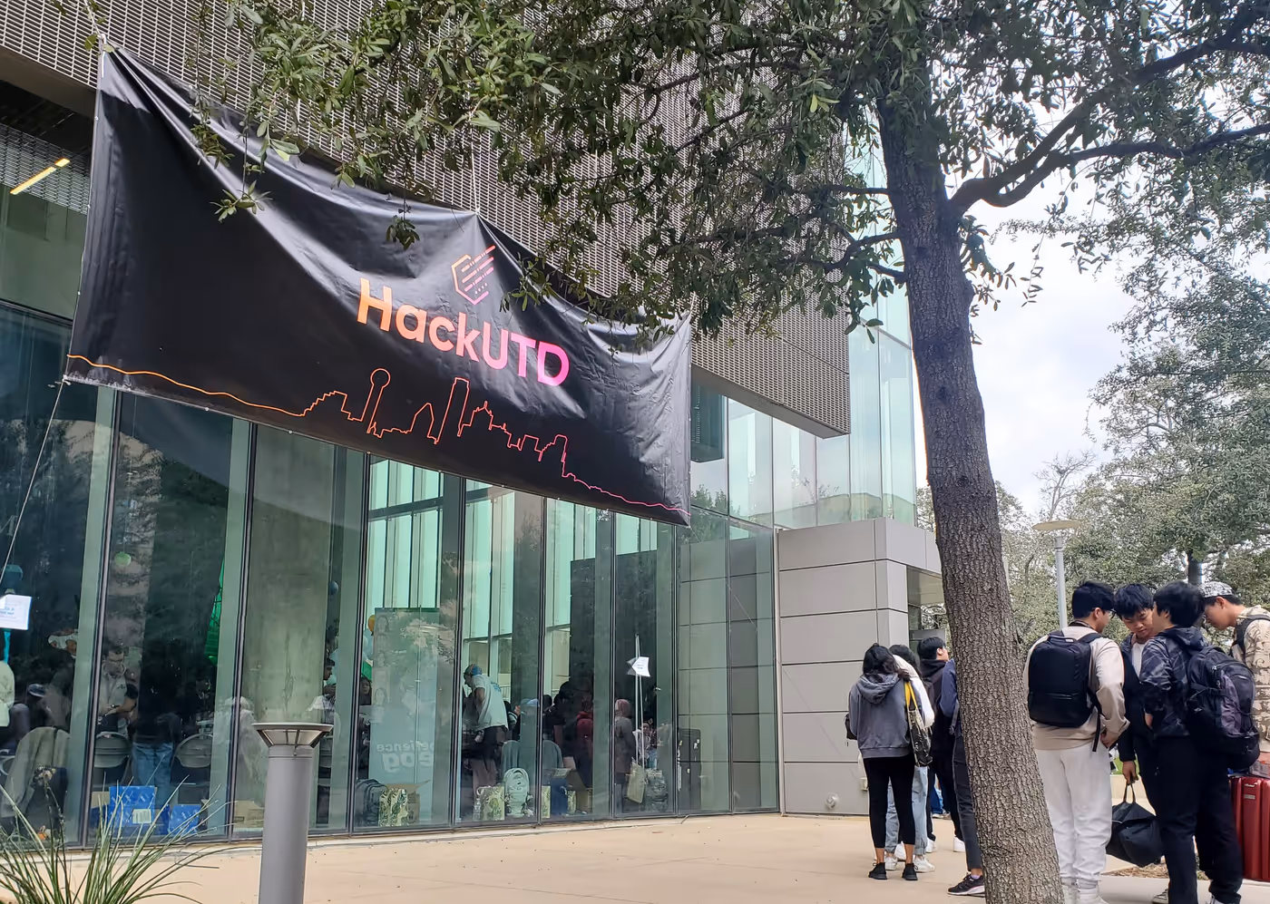 glass-walled university building with large HackUTD banner suspended over vestibule